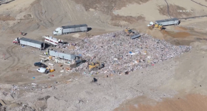 A photo of the Chiquita canyon Landfill taken from a drone showing three large dump trucks around a enormous pile of garbage.